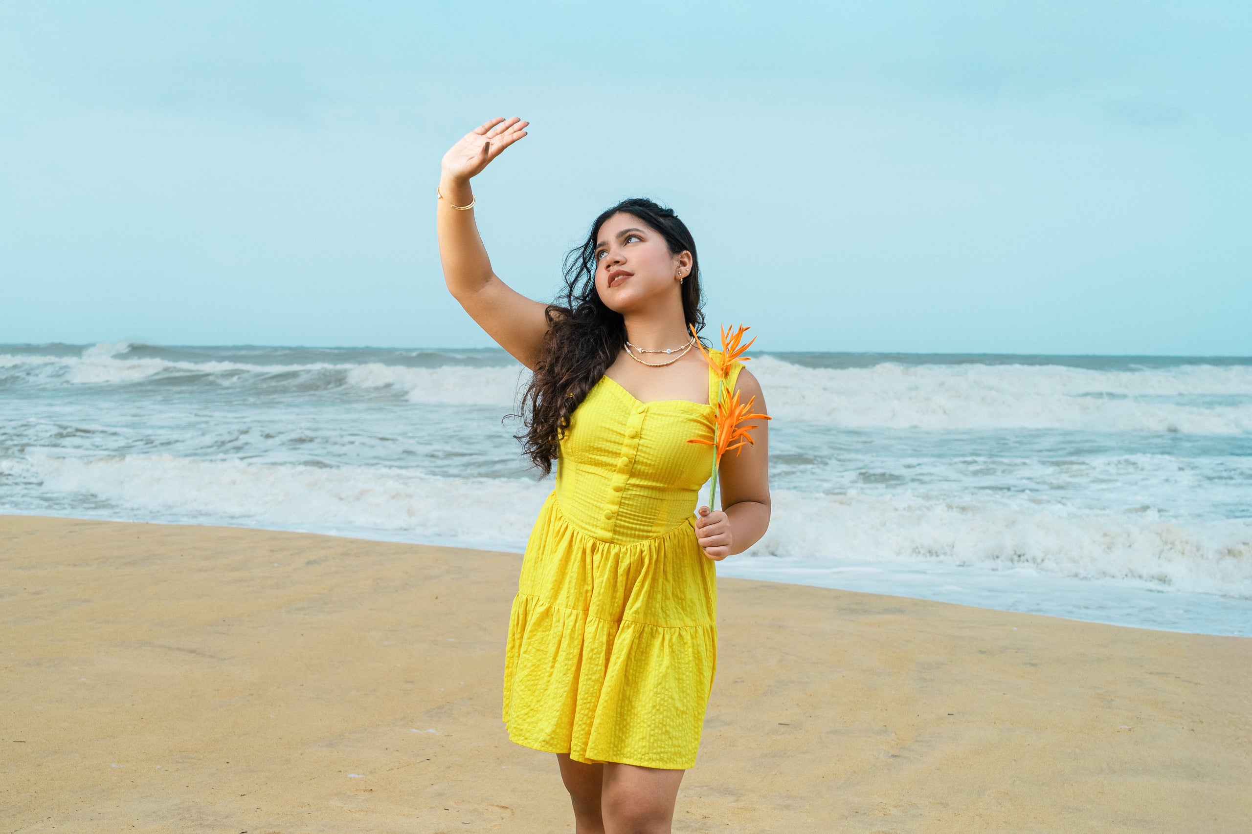 Woman in a yellow dress on a beach with ocean waves in the background