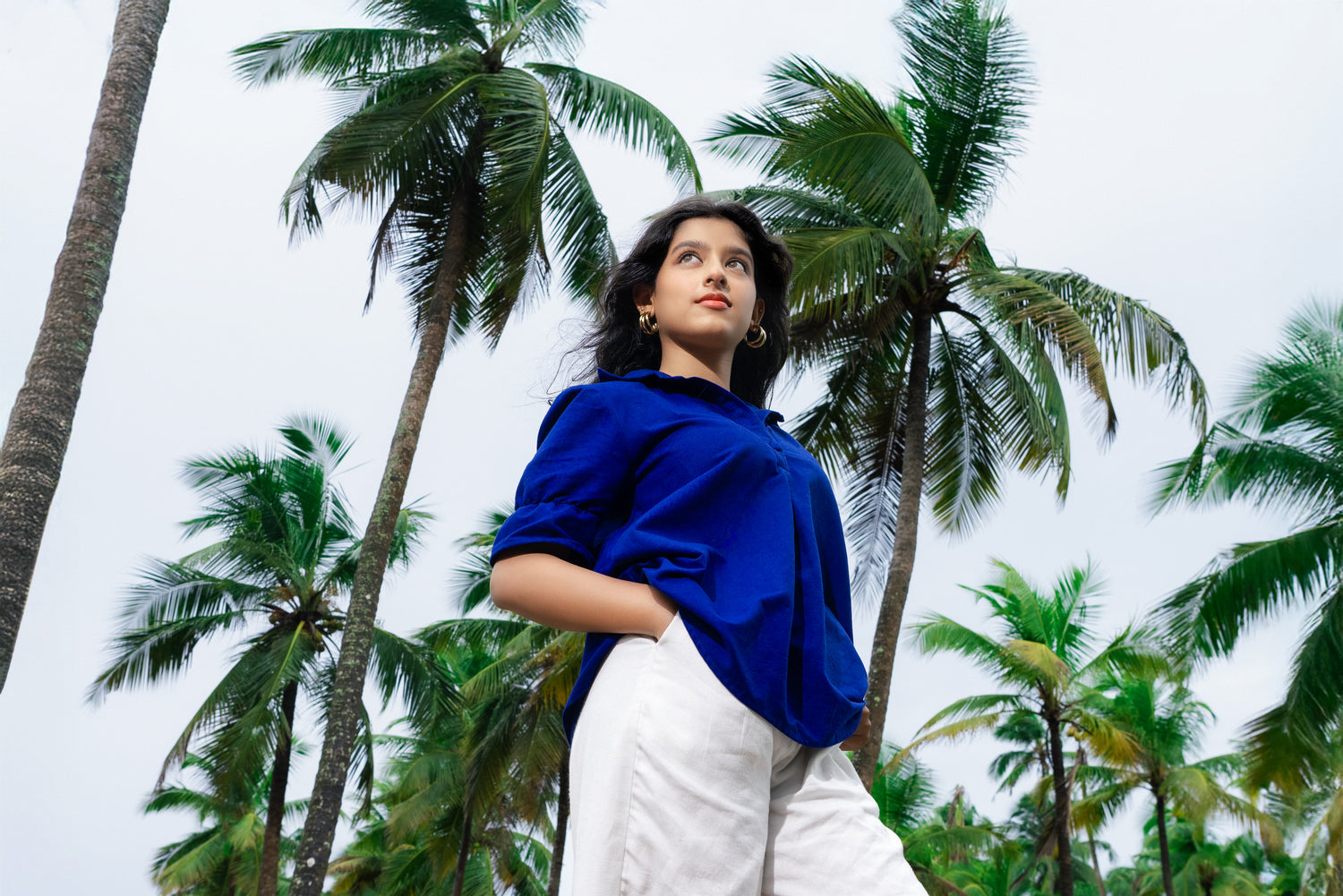 Woman in a blue top and white pants standing among palm trees
