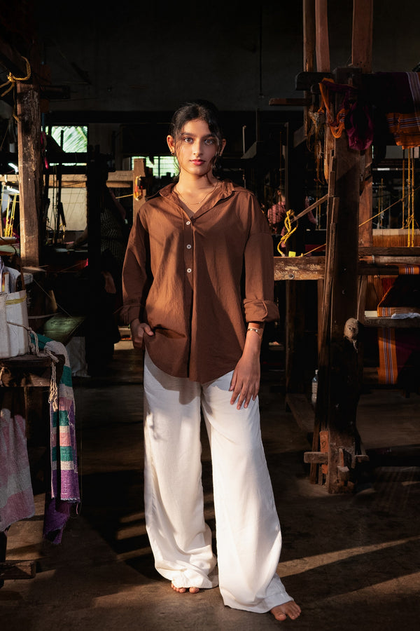 Woman wearing a brown blouse and white pants standing in a weaving shed.
