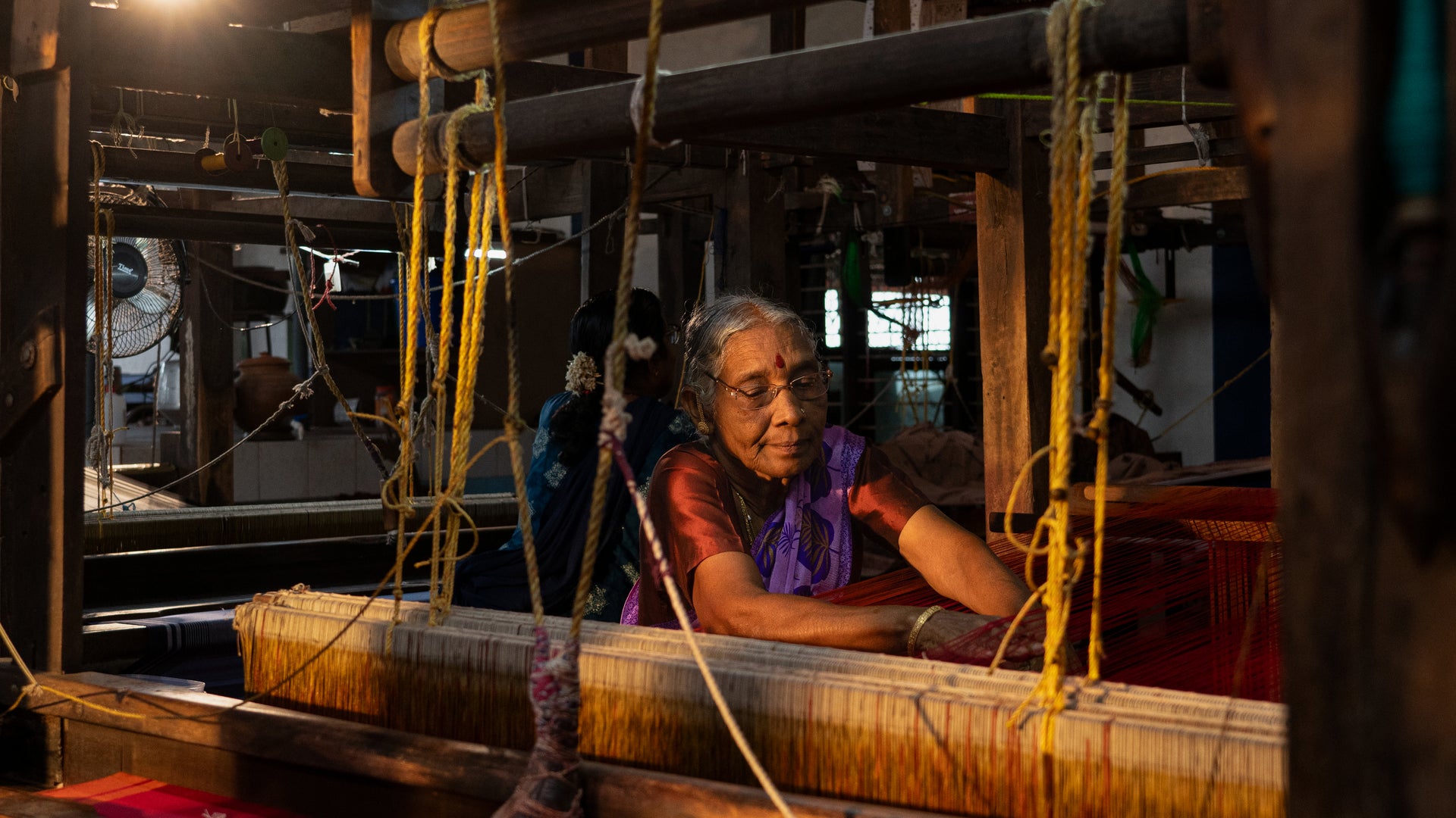 Woman operating a traditional loom in a dimly lit room