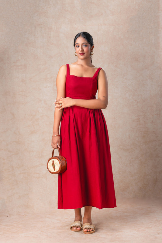 Woman wearing a red dress holding a round bag against a beige background