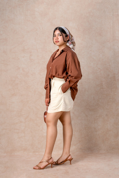 Woman wearing a brown shirt and white shorts against a beige background