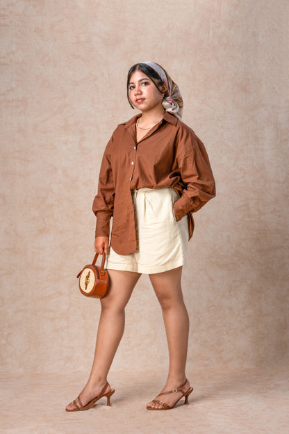 Woman wearing a brown shirt and white shorts against a beige background