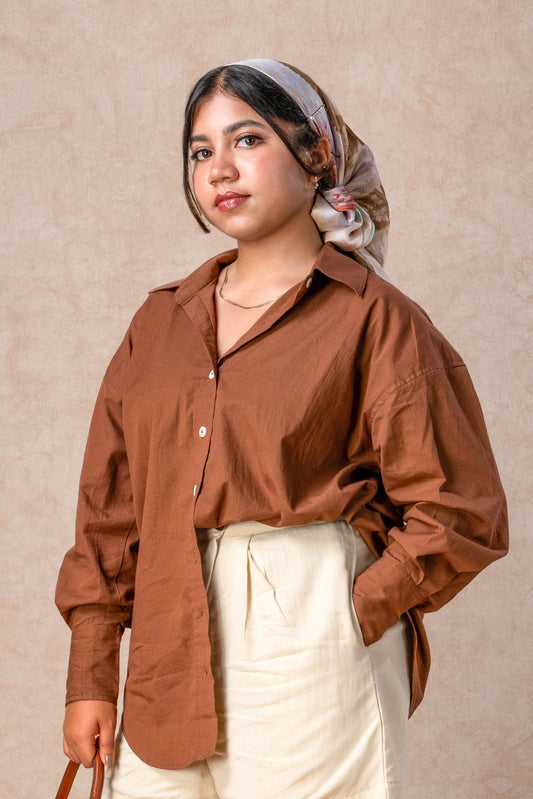 Woman wearing a brown shirt and white pants against a beige background