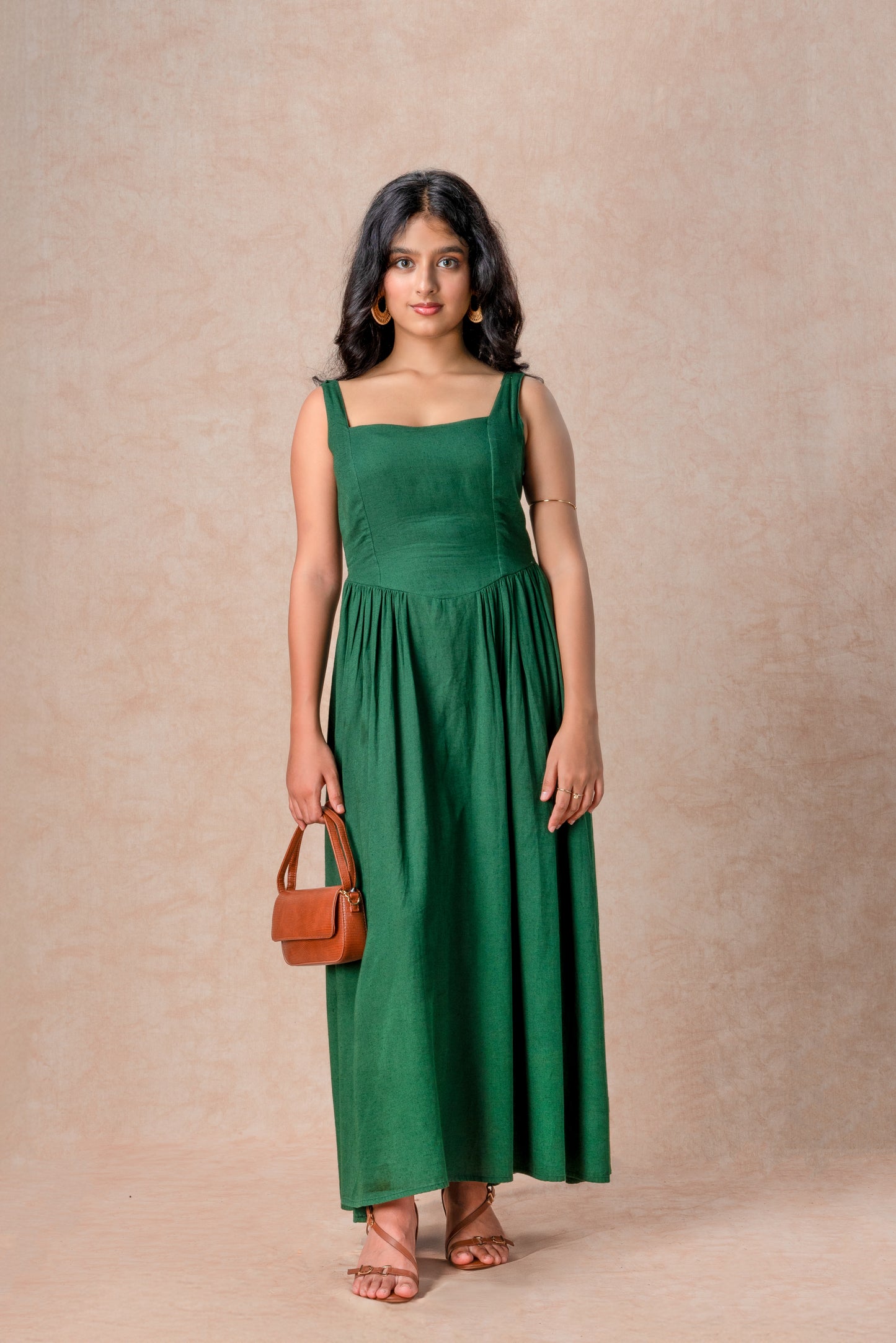 Woman wearing a green dress holding a brown handbag against a beige background