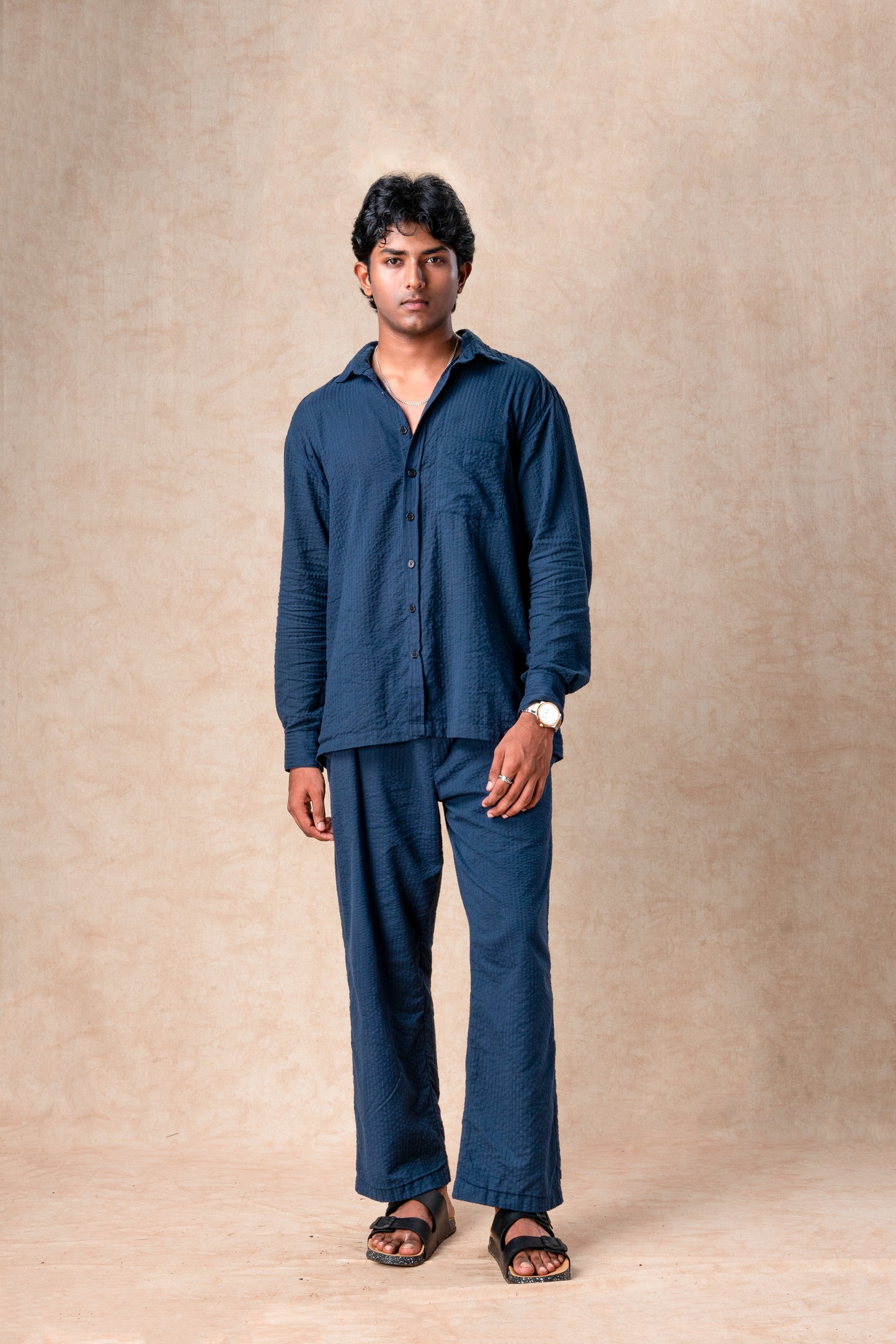 Man wearing a blue shirt and pants against a beige background