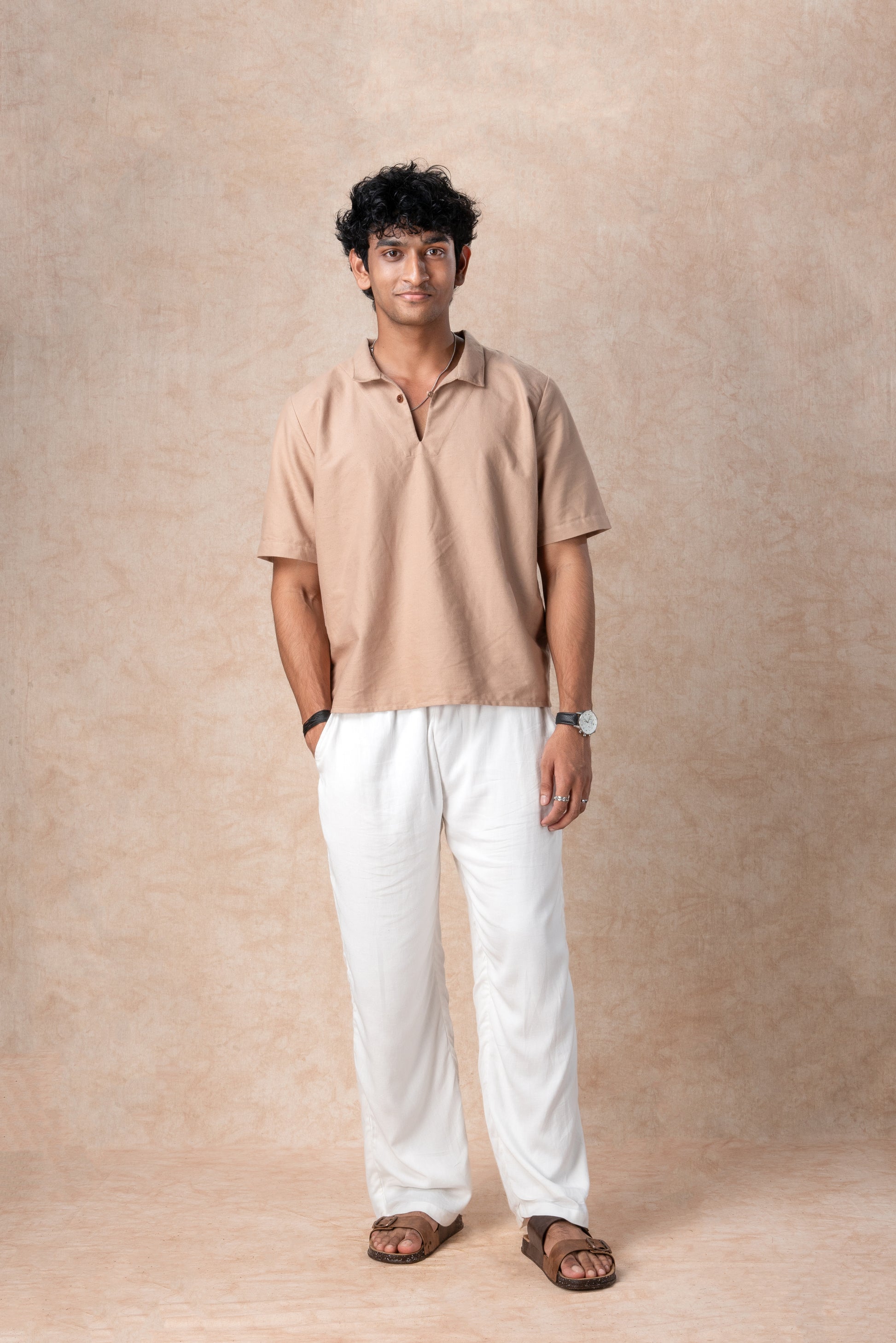 Man wearing a beige shirt and white pants against a beige background