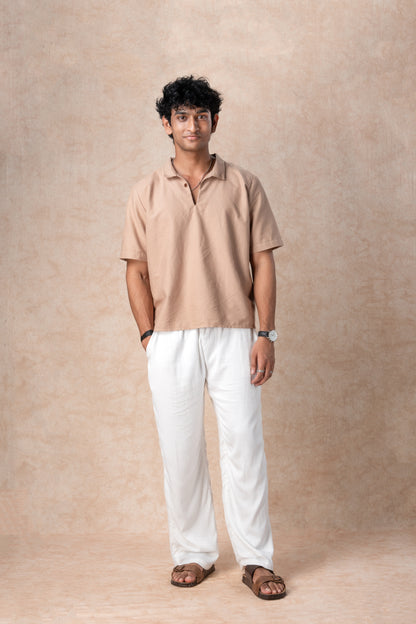 Man wearing a beige shirt and white pants against a beige background