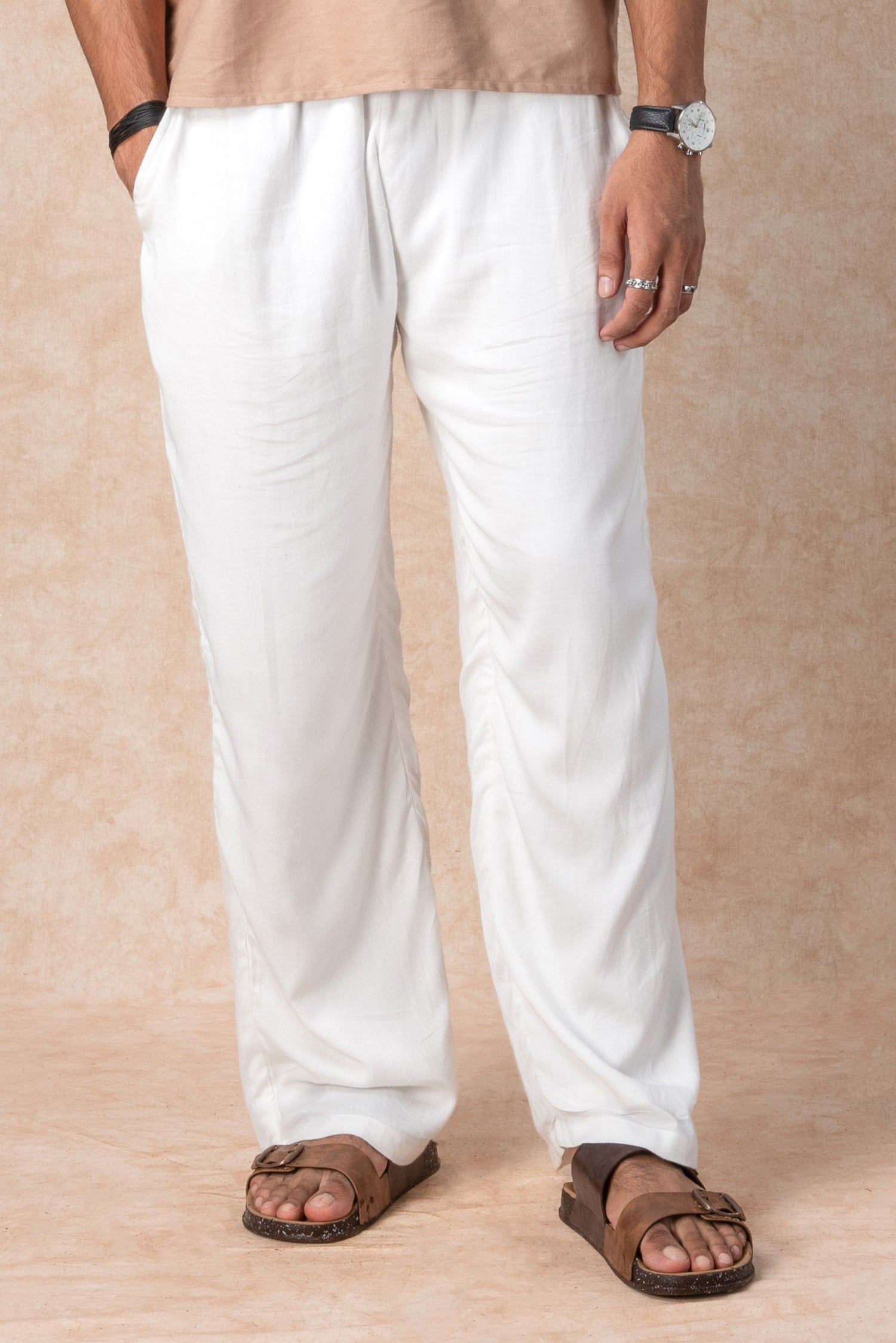 Person wearing white dhoti pants and brown sandals on a beige background