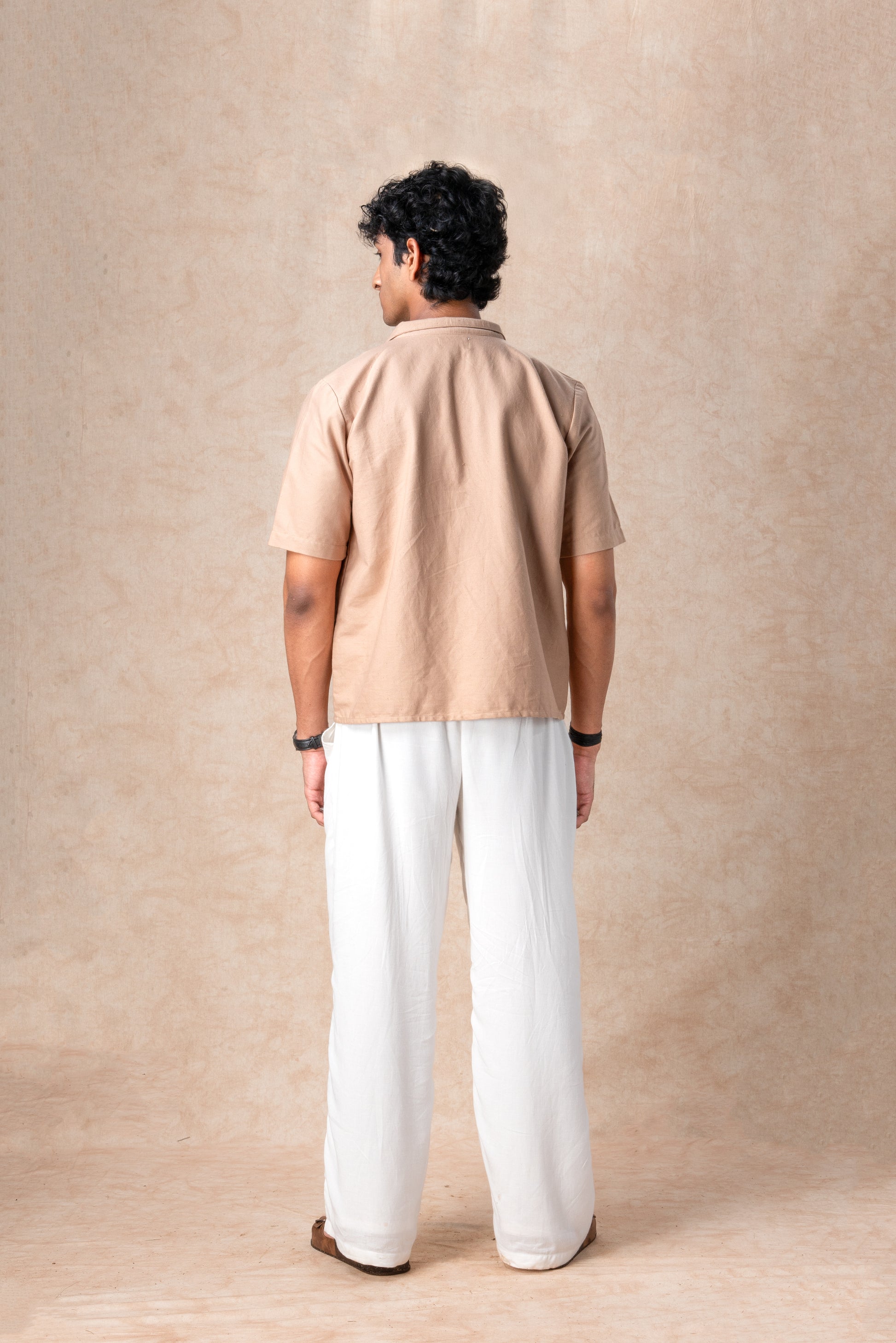 Person wearing a beige shirt and white pants against a beige background