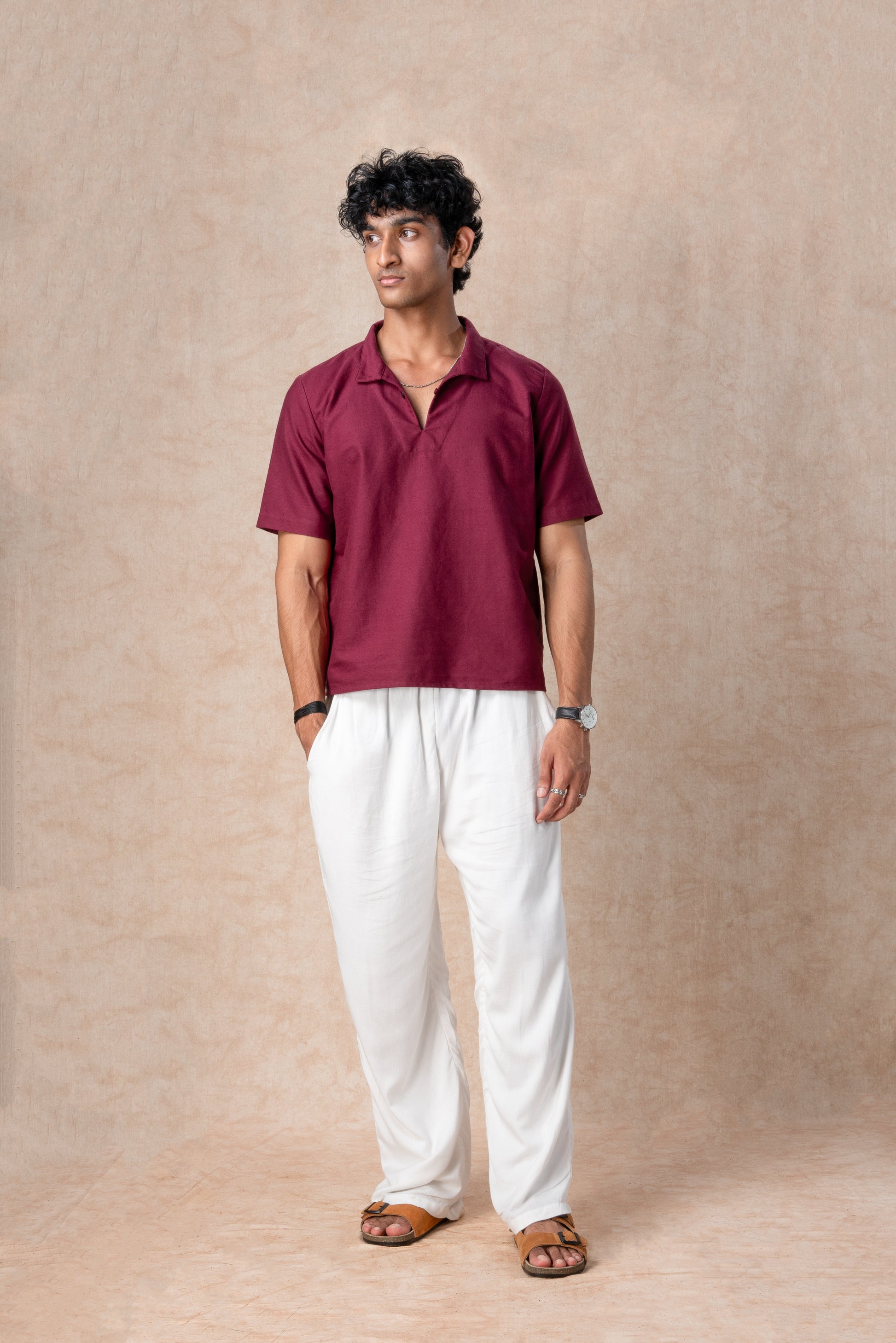 Man wearing a maroon shirt and white pants against a beige background