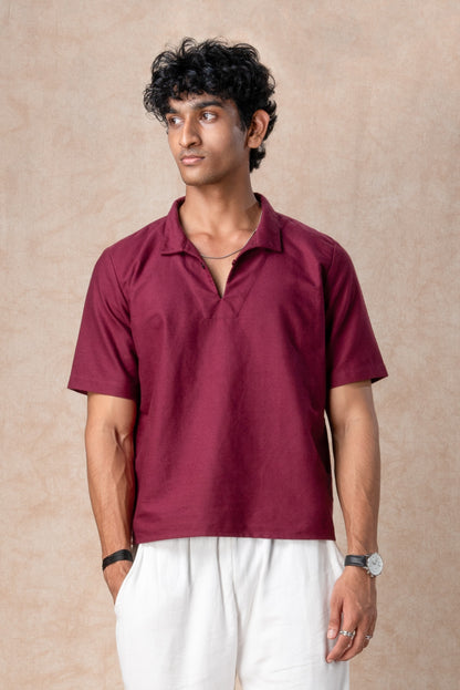 Man wearing a maroon polo shirt and white pants against a beige background