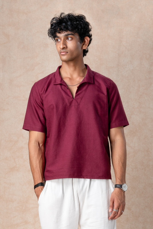 Man wearing a maroon polo shirt and white pants against a beige background