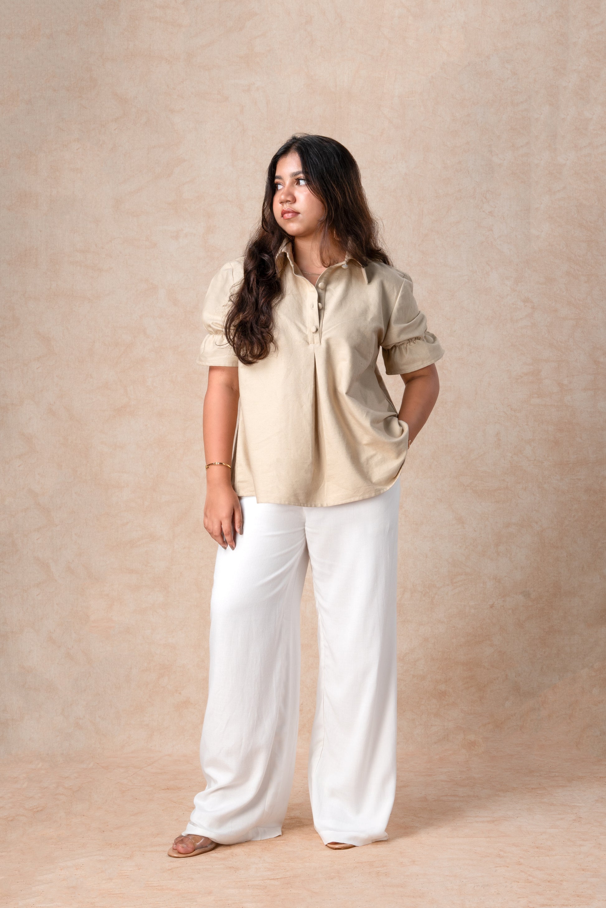 Woman wearing a beige shirt and white pants against a beige background