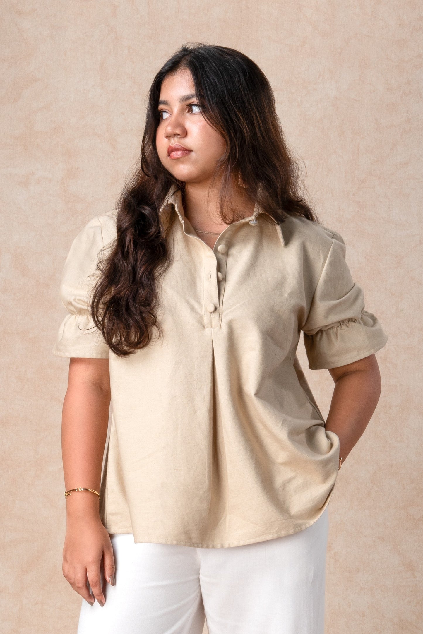 Woman wearing a beige shirt and white pants against a beige background