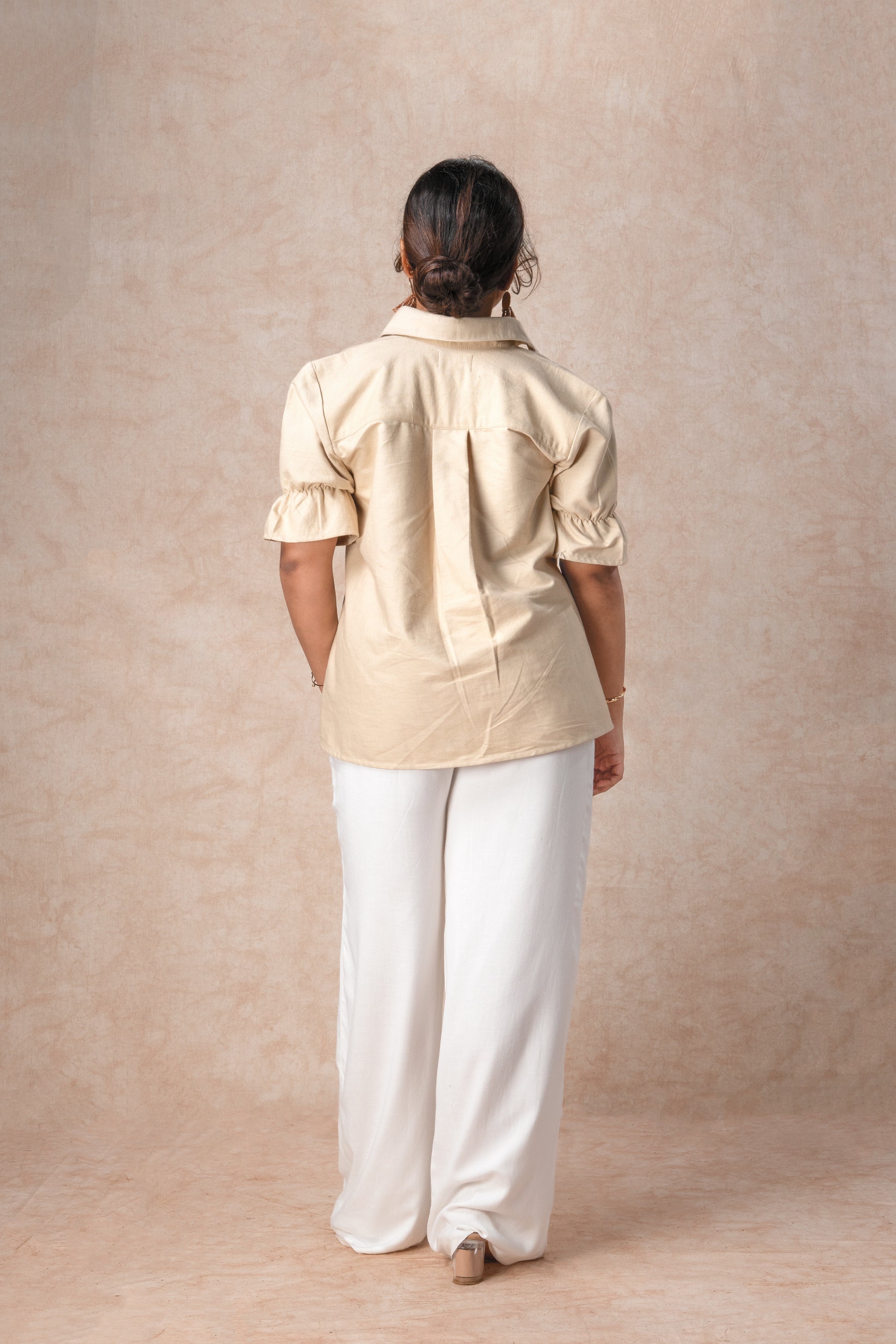 Person wearing a beige shirt and white pants against a beige background