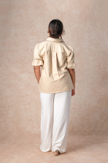 Person wearing a beige shirt and white pants against a beige background