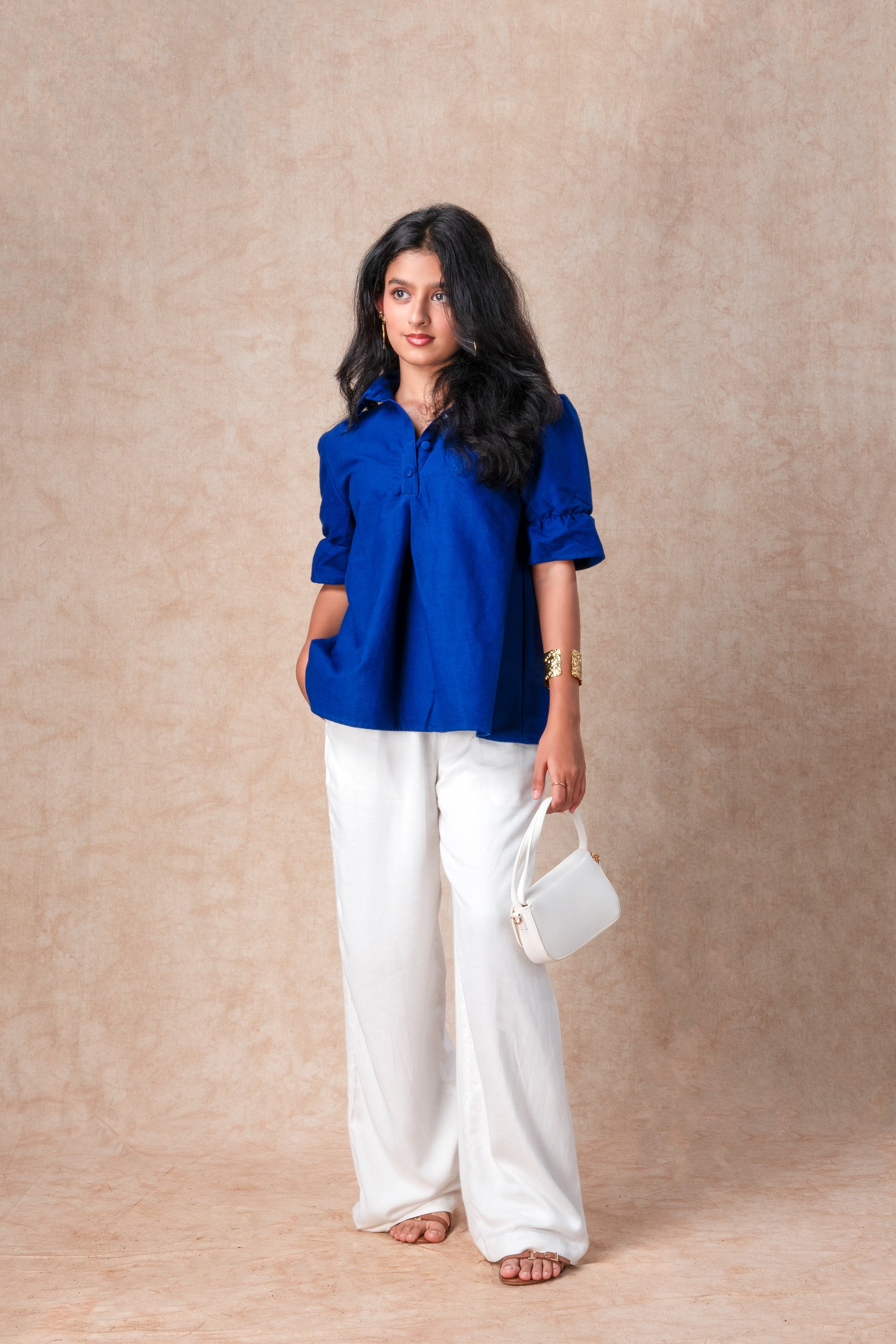 Woman wearing a blue shirt and white pants against a beige background