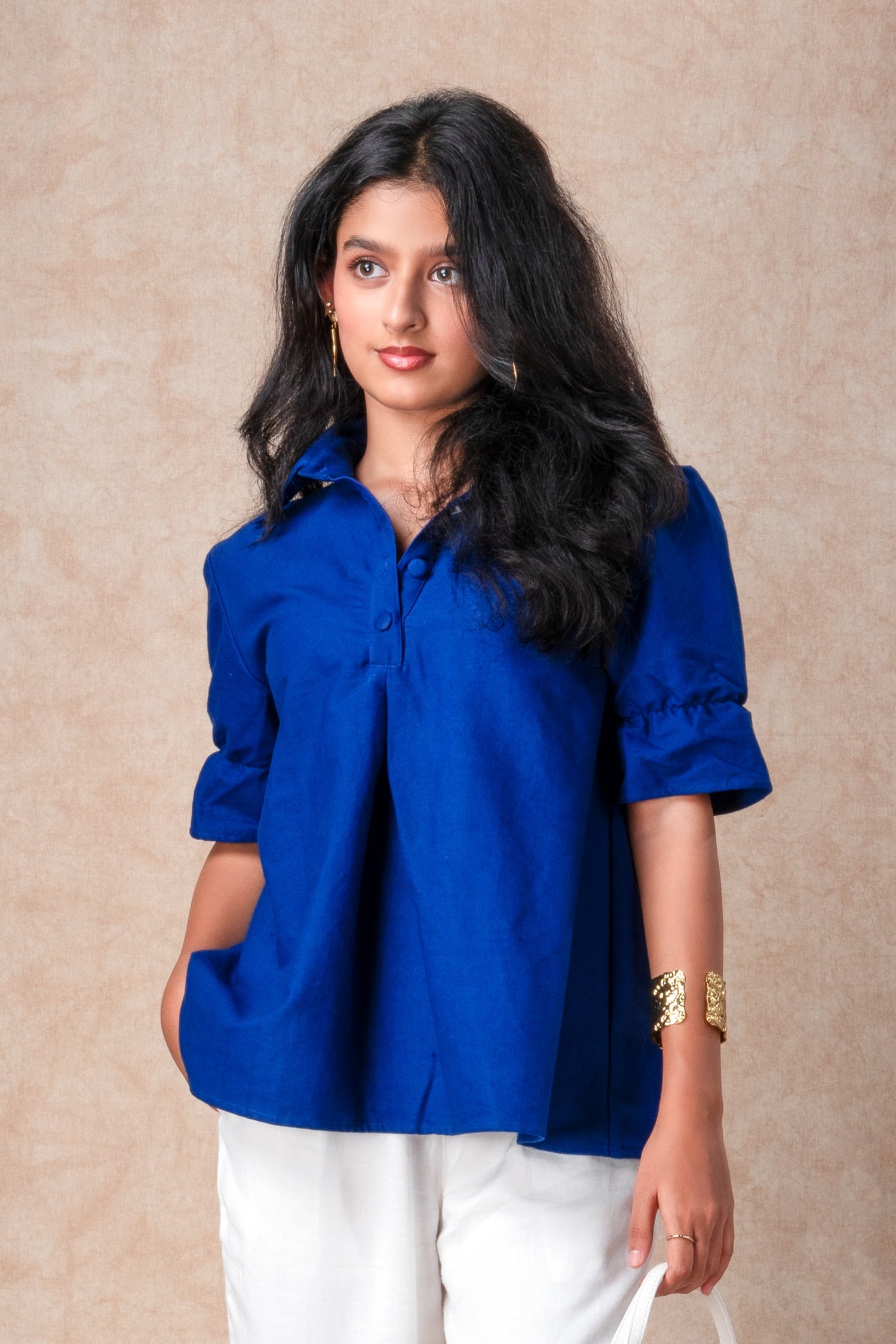 Woman wearing a blue shirt and white pants against a beige background