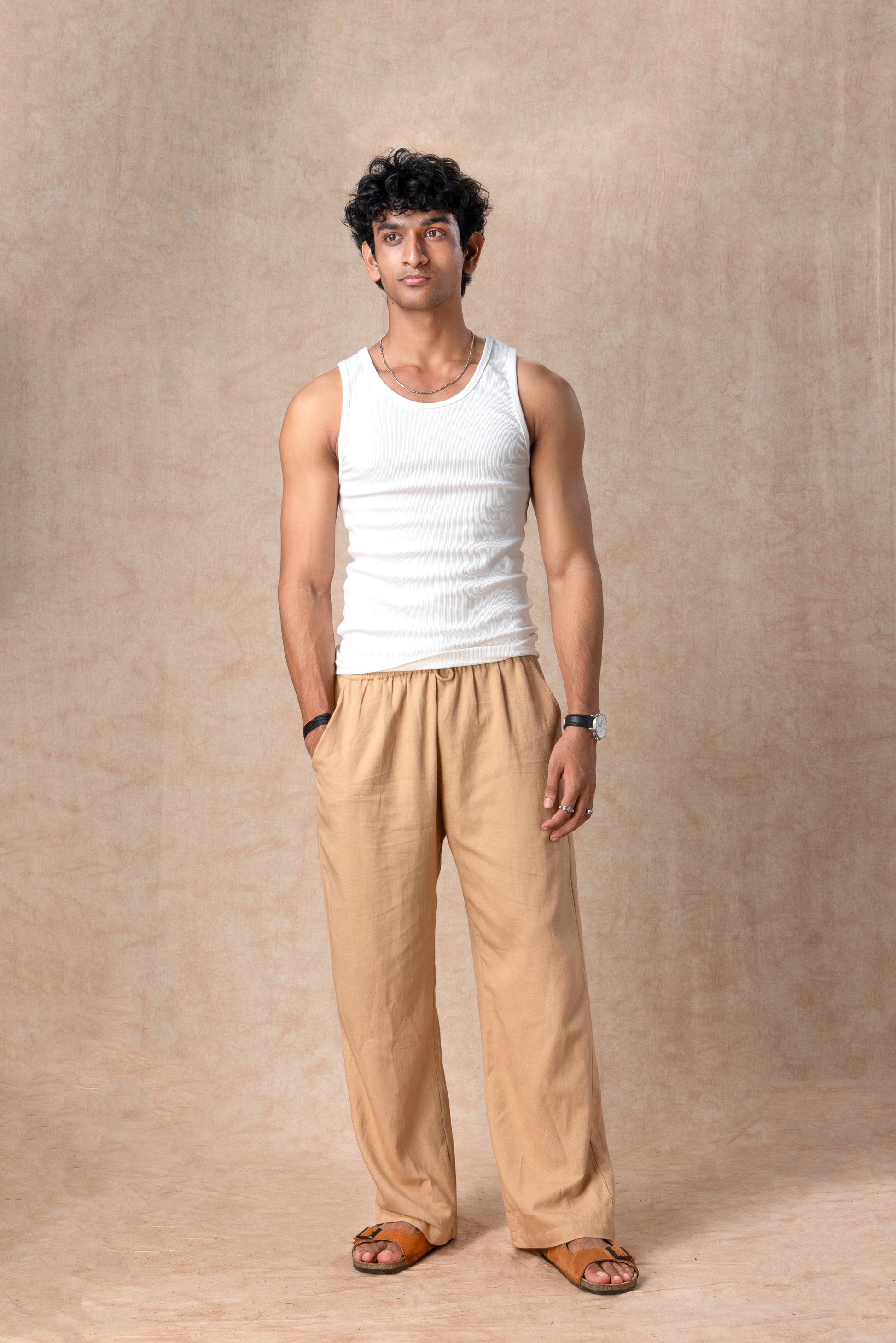 Man wearing a white tank top and beige pants against a beige background