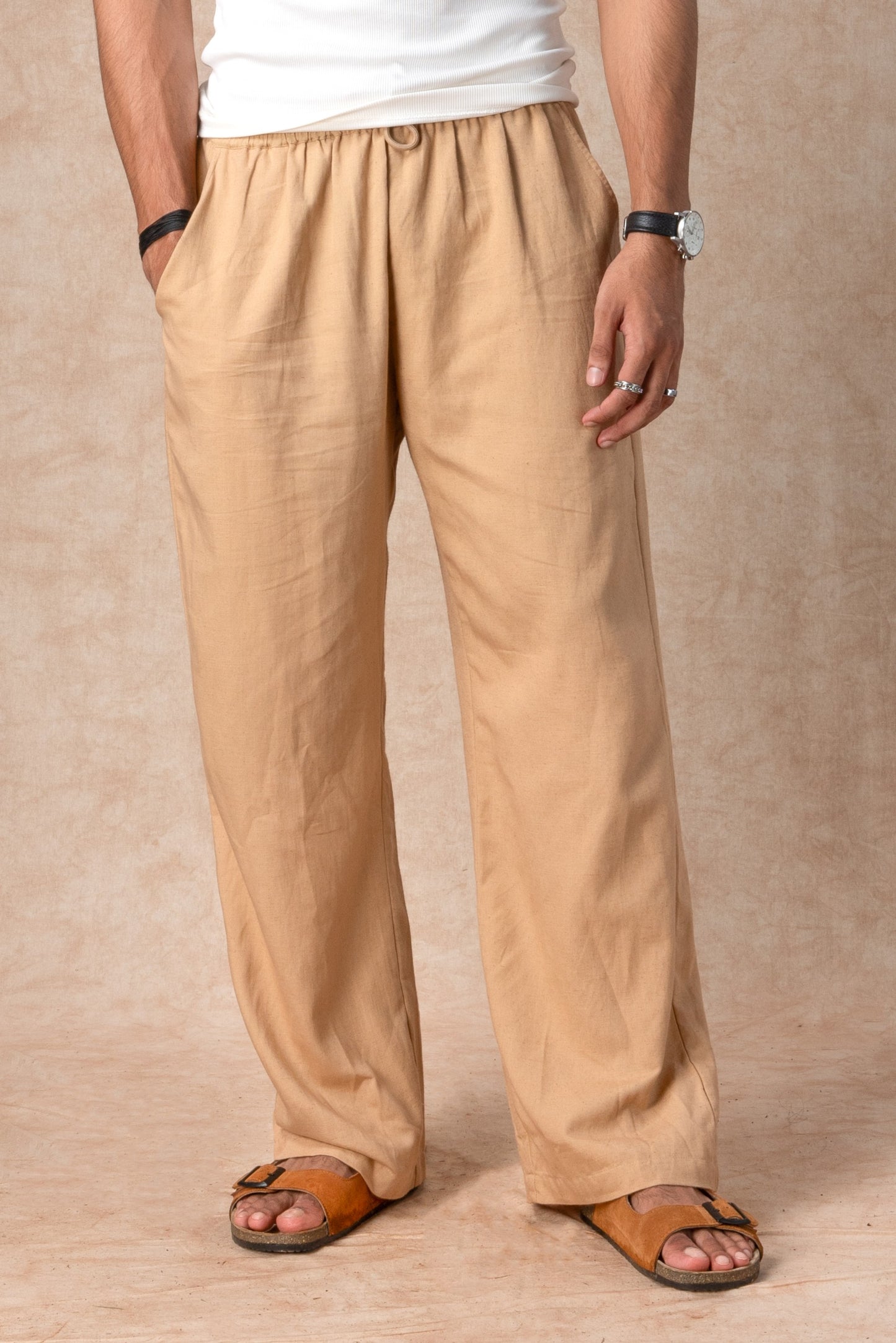 Person wearing beige pants and brown sandals against a beige background