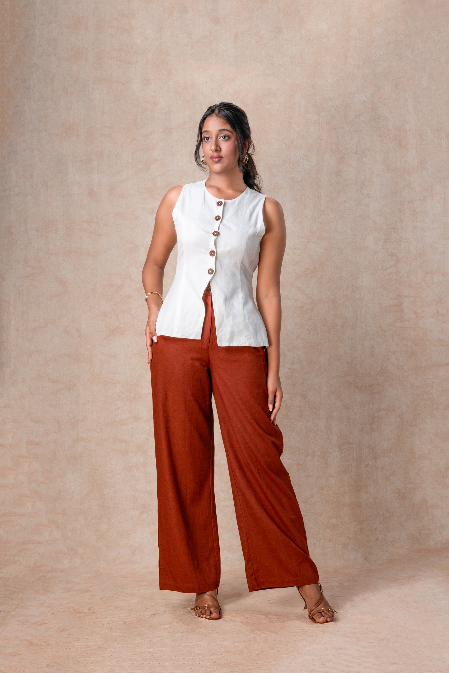 Woman wearing a white sleeveless top and rust-colored pants against a beige background