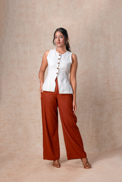 Woman wearing a white sleeveless top and rust-colored pants against a beige background