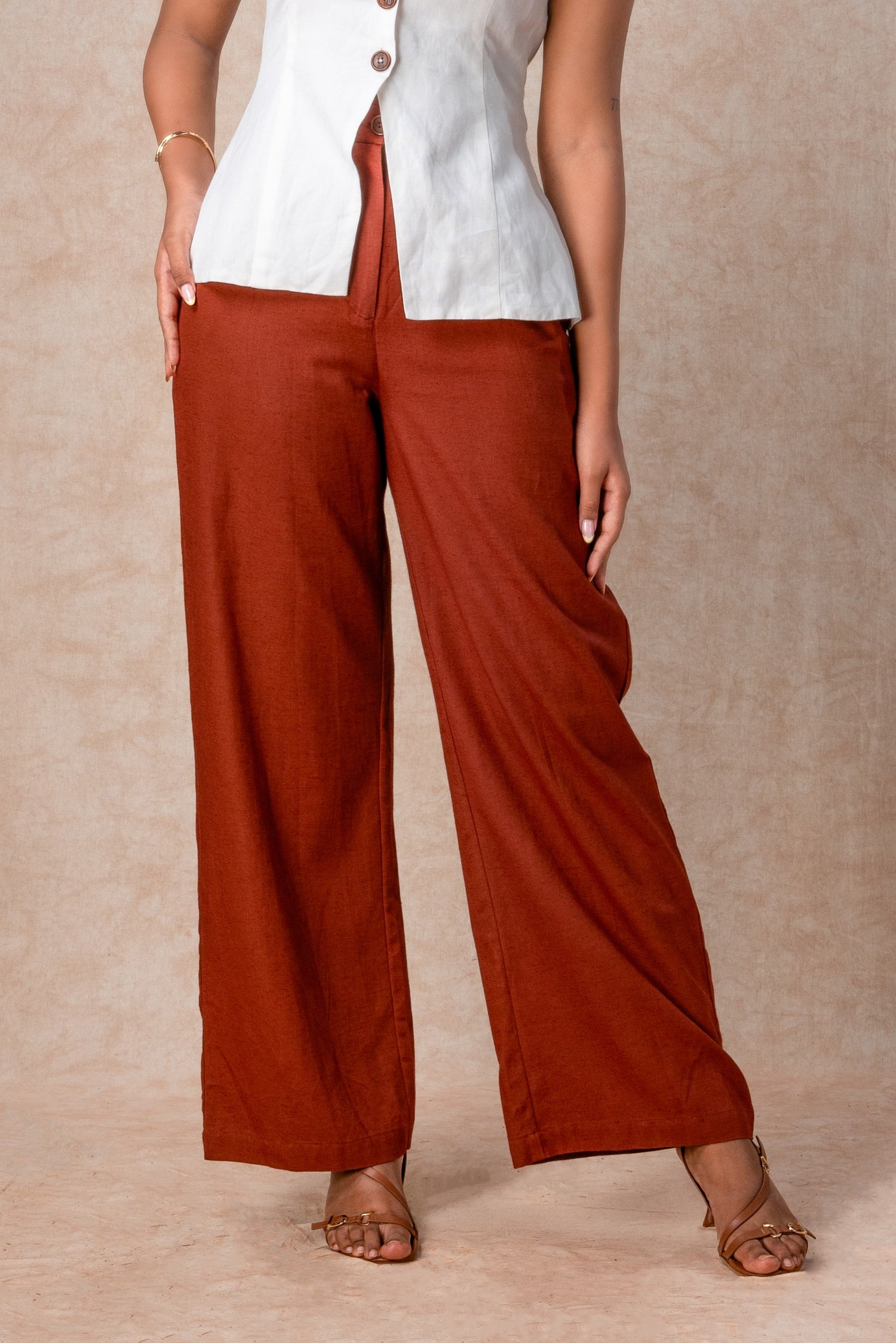 Person wearing rust-colored wide-leg pants and a white top on a beige background