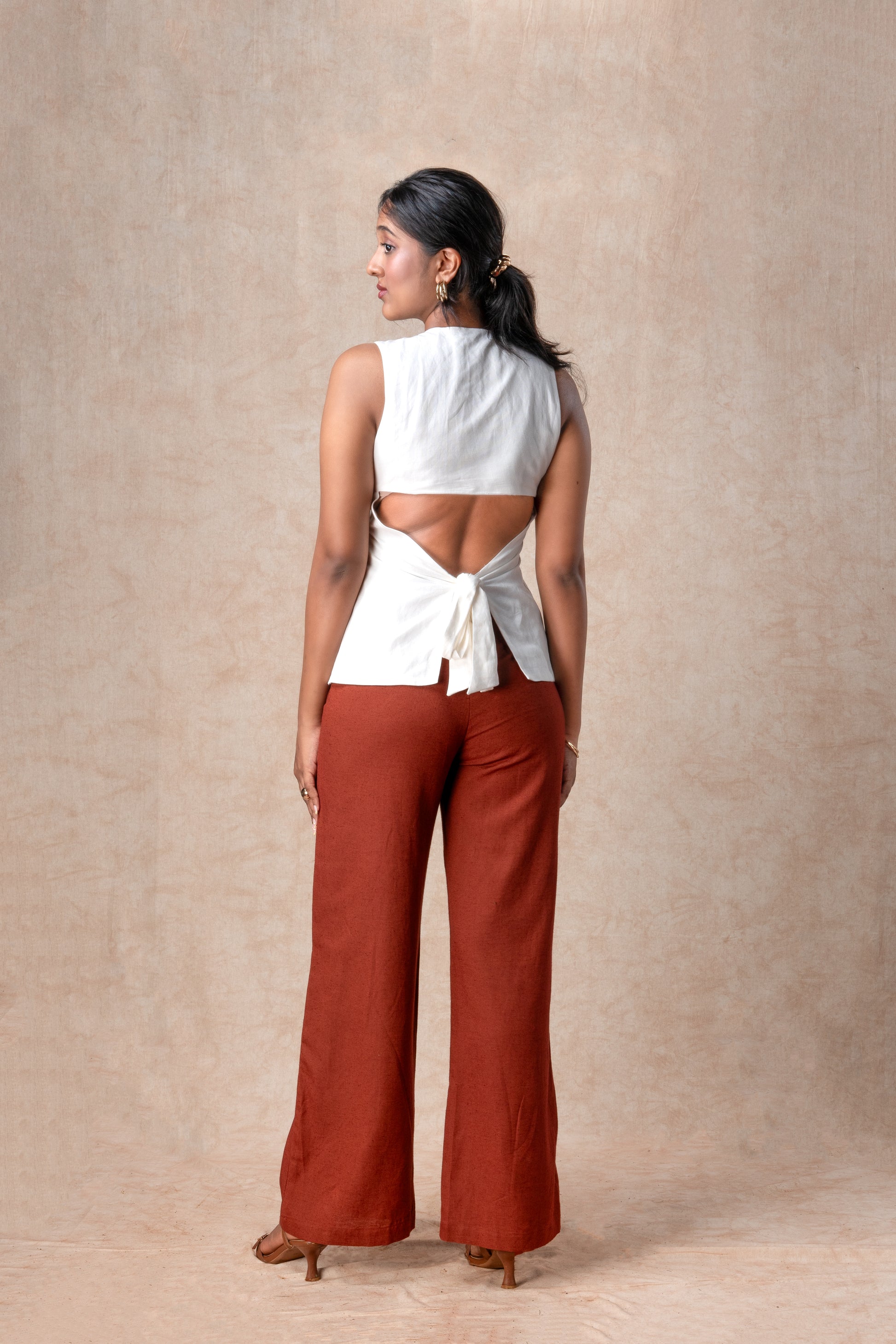 Woman wearing a white top and rust-colored pants against a beige background